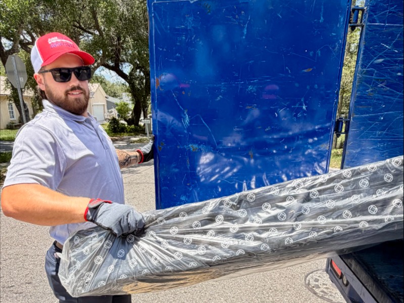 Junk Nation Removal team member loading a shrink-wrapped mattress into the trailer