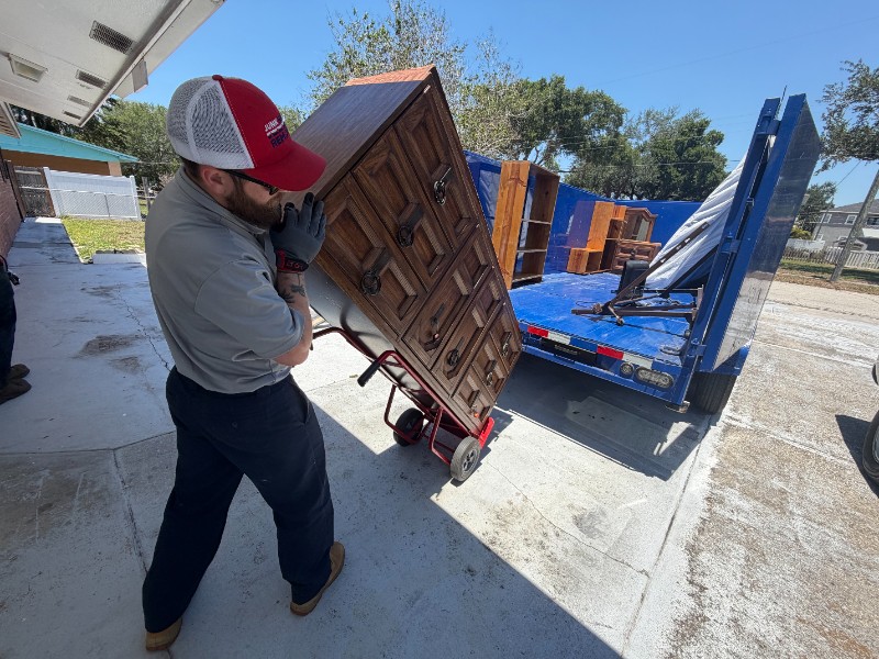 Junk Nation Removal team member moving a wooden dresser by dolly to the trailer