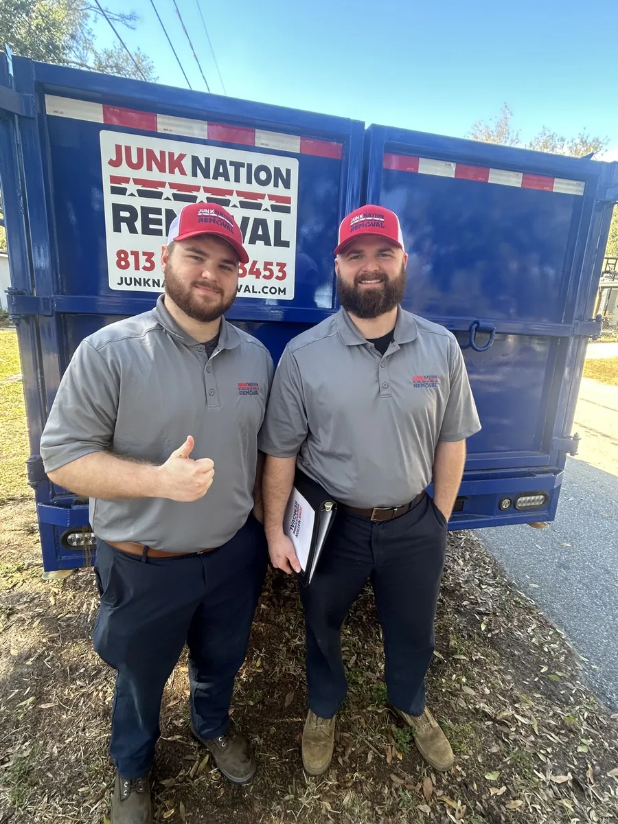 Two Junk Nation Removal crew members standing in front of a loaded junk removal trailer