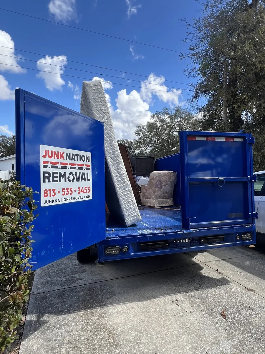 Junk Nation Removal trailer loaded with an old mattress and armchair outside a Tampa Bay home